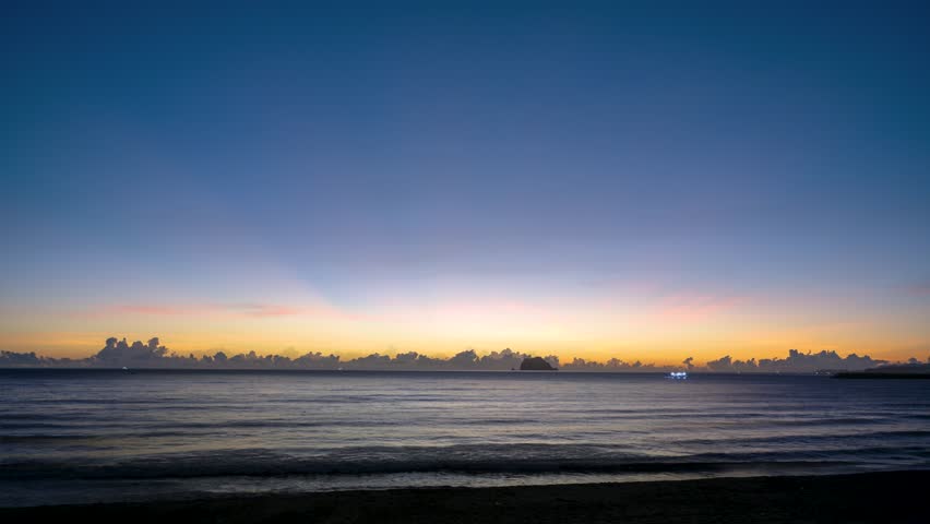 Stunning wide shot of crepuscular rays shooting into the blue and purple sky over the rocky coastline and ocean during pre sunrise in Wanli District New Taipei City Taiwan.