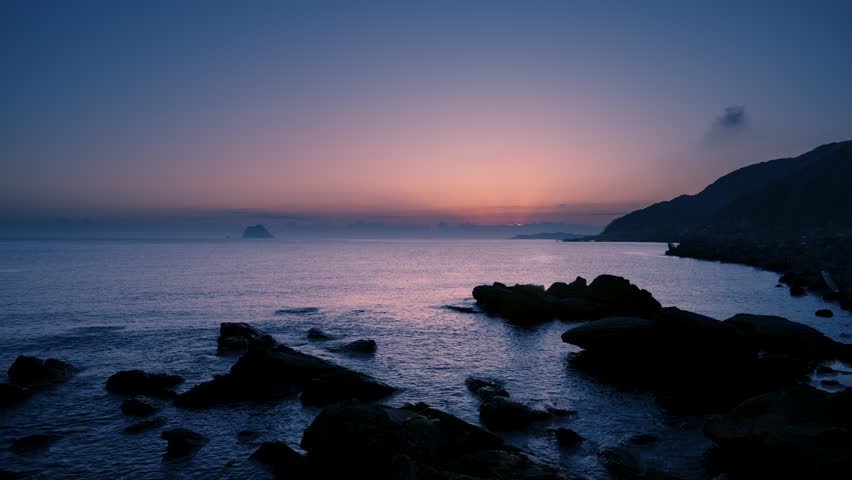 Beautiful scenic shot of the sun slowly rising over the ocean horizon at dawn near Dawulun Fishing Port Keelung Taiwan The foreground features dark rocks and Keelung Islet silhouette.