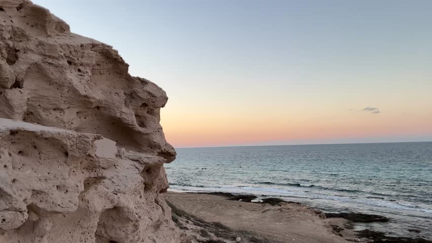 “Golden-hour view of a rocky beach, ocean waves, and dramatic cliff formations.”