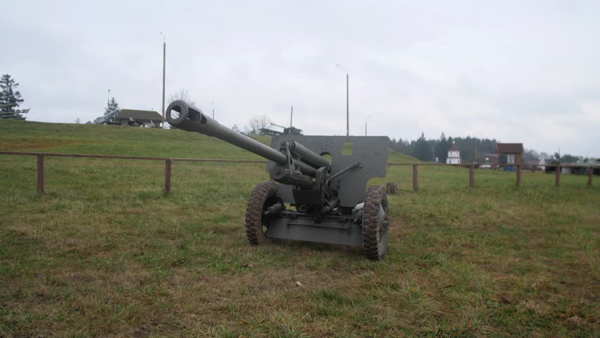 towed howitzer cannon positioned on open pasture with long barrel angled toward sky, visible carriage wheels and muzzle, historic training ground atmosphere; scene includes rural landscape,