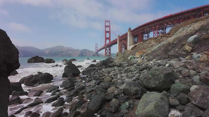 Waves roll onto sandy shore at Baker Beach with Golden Gate Bridge in background, San Francisco, California, USA. Iconic coastal view with ocean, rocks and Marin Headlands