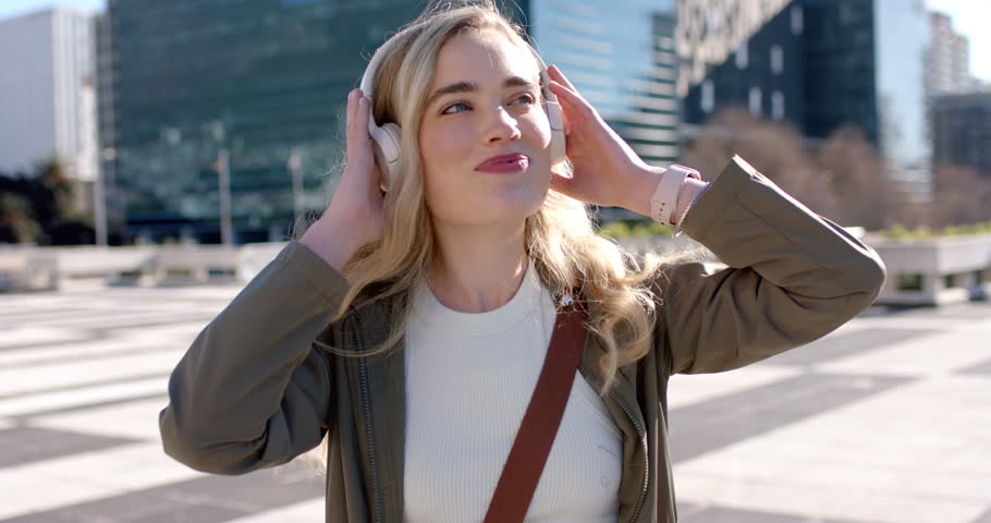 Entering plaza, woman raising headphones, bobbing to rhythm, removing headphones to admire skyline. Urban, lifestyle, modern, fashion, leisure, vibrant, upbeat