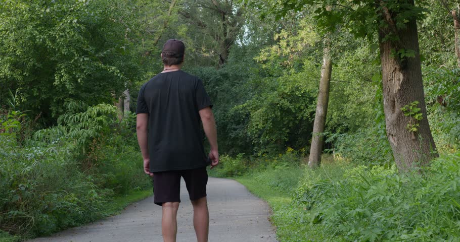 A man walks along path in green spring forest, limping on one leg