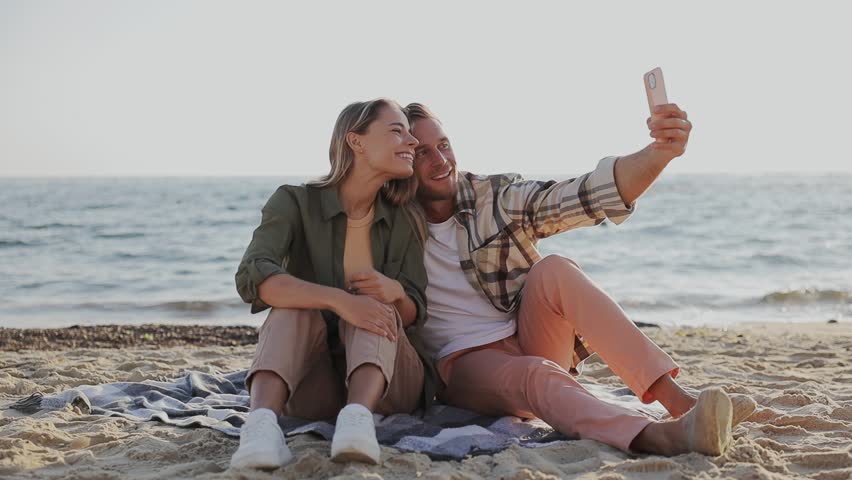 Full body young couple two friends family man woman wear shirt casual clothes sit do selfie shot on mobile cell phone rest relax in free time walk on sea ocean sand shore beach seaside in summer day