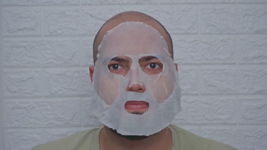 Man Usinf Jade Roller with Sheet Mask on Face