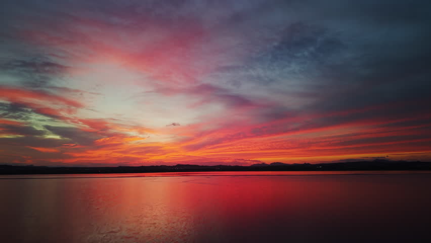 Vivid sunset over a tranquil salt lake reflecting red, orange, and purple hues under a dramatic sky. High quality 4k footage