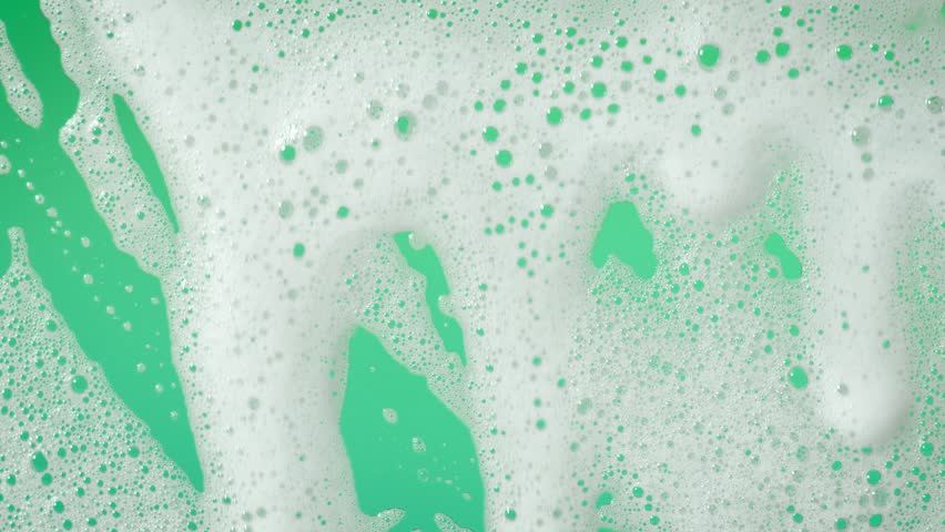 A slow-motion close-up of white soap foam gracefully flowing and drifting across a soft gray and white surface, creating a calming and clean aesthetic.