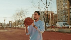 Slow motion shot of a cheerful young man spinning a basketball effortlessly on his finger beneath glowing golden-hour sunlight on a bright urban court. - Powered by Shutterstock - Get 15% off with code: PIKWIZARD15