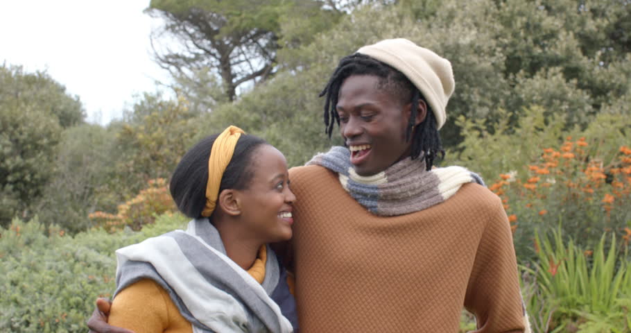 African American couple entering garden of orange blooms, putting arm around her, smiling, laughing. Romantic, outdoor, botanical, affectionate, joyful, candid, natural