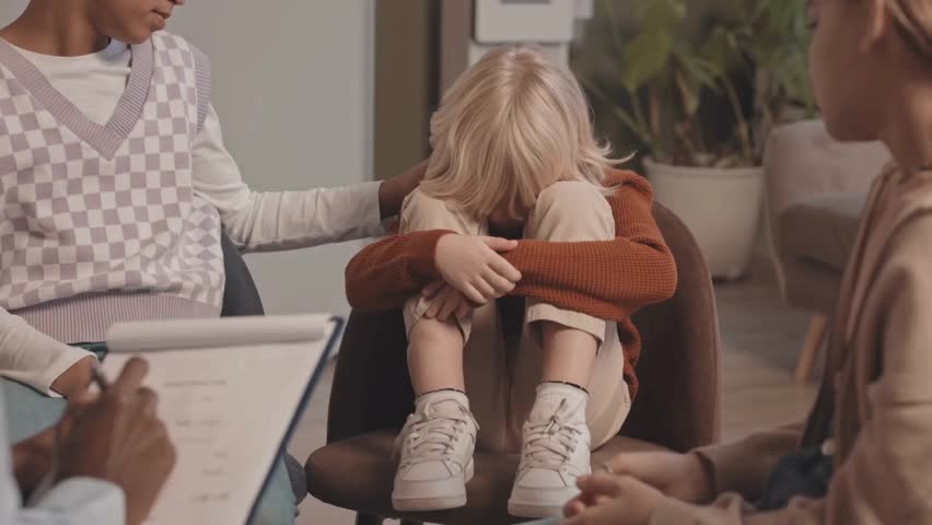 A slow-motion scene of a young boy crying while the therapist and girls in the group gently comfort him during a supportive therapy session.

