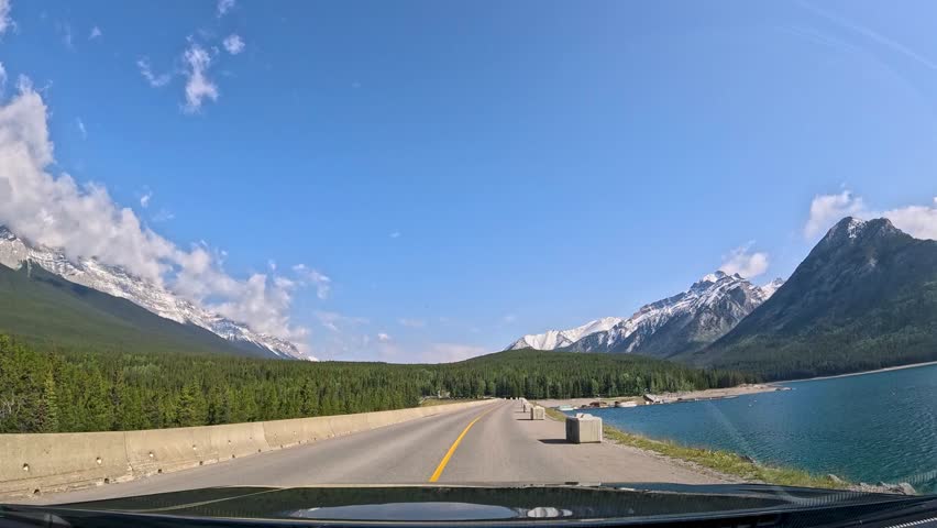 Scenic drive through Banff Canada showcasing stunning mountains and clear lakes on a sunny day. Enjoy a breathtaking drive through Banff Canada, surrounded by majestic mountains and beautiful lakes un
