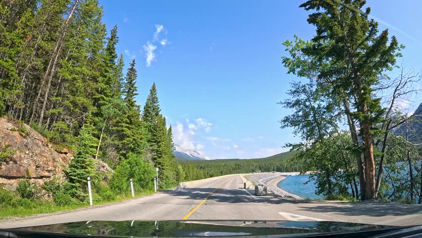 Scenic drive through Banff Canada showcasing stunning mountains and clear lakes on a sunny day. Enjoy a breathtaking drive through Banff Canada, surrounded by majestic mountains and beautiful lakes un