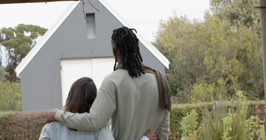 Diverse couple walking into garden, wrapping arms around waists and admiring new grey cabin doors. Romantic, intimacy, serenity, architecture, tranquility, nature, lifestyle