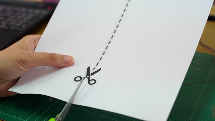 A close-up view of a hand holding scissors and cutting through paper, showcasing a dotted line as a guide. This image captures the essence of creativity and craft.