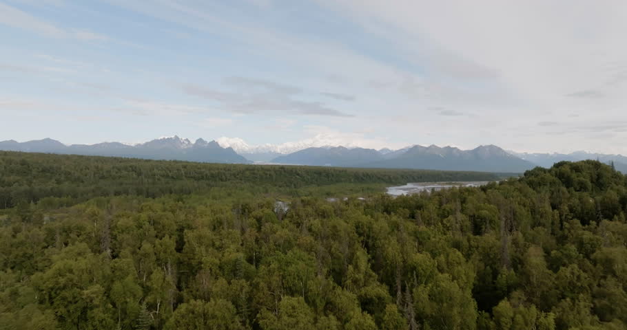 Aerial above dense forest and Susitna River with view of high mountains range in the background, North America