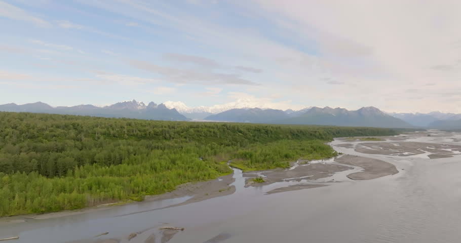 Flying sideways above forest and Susitna River with high mountains in the background, Alaska