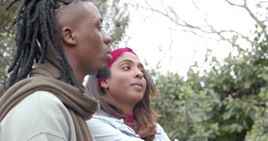 African American man smiling encouraging Indian woman in leafy park grinning and pointing. Connection, diversity, friendship, nature, candid, outdoor, joyful