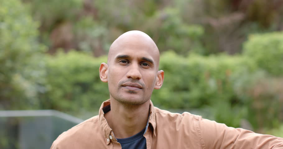 Asian man wearing tan shirt by metal railing in backyard noticing camera and smiling and laughing. Outdoor, leisure, relaxation, greenery, candid, natural, approachable