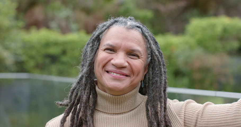Facing camera extending arm holding smartphone, senior woman laughing while recording garden moment. Joyful, authentic, candid, natural, vibrant, leisure, outdoor