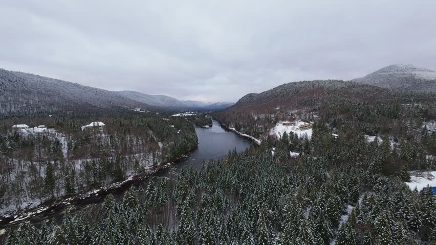 Low sweeping cinematic shot across icy riverbanks framed by towering mountains covered in pure untouched snow.