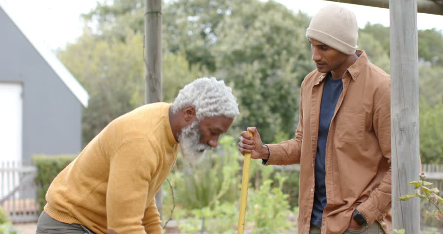 Senior male friends spotting, clearing weeds for seedling health in garden bed using trowel and hoe. Gardening, horticulture, outdoor, partnership, cultivation, nature, vitality