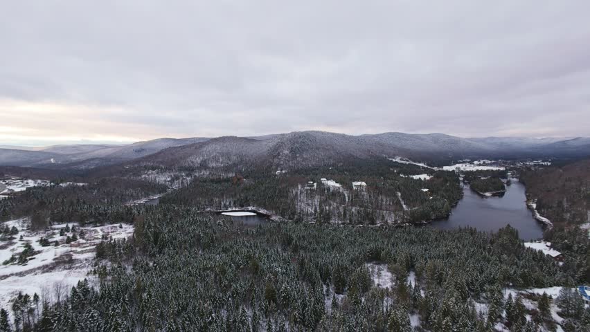 Aerial winter drift revealing a tall mountain ridge stretching across a vast snowy plains with a reflective icy river cutting through.