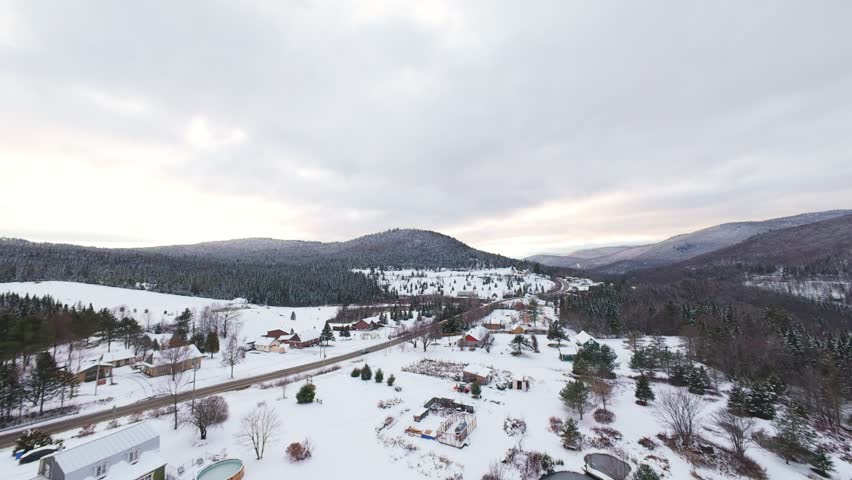 Aerial descent toward a narrow snowy canyon carved by a dark reflective river flowing between steep winter slopes.