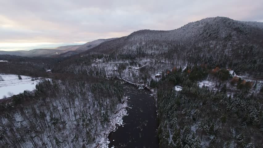 Aerial cinematic drift alongside a snowy ridge with a river cutting diagonally across the valley. Clean luxury winter composition with smooth color gradients.