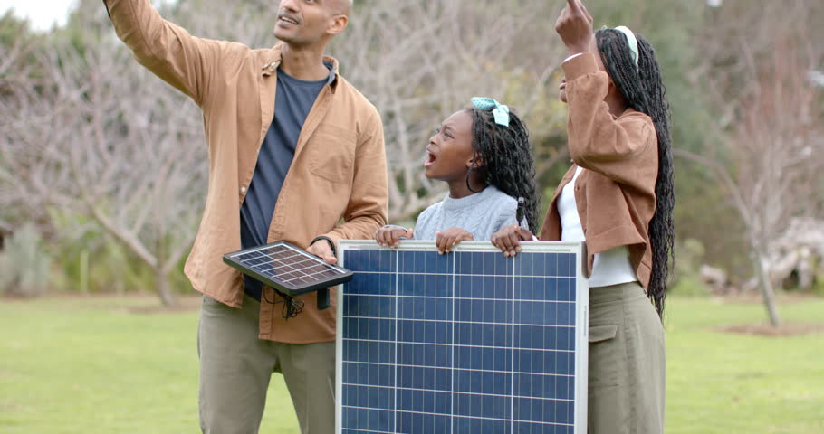 Diverse family father explaining solar power with small panel as daughters adjusting panel in yard. Sustainable, education, environment, renewable, innovation, technology, outdoor
