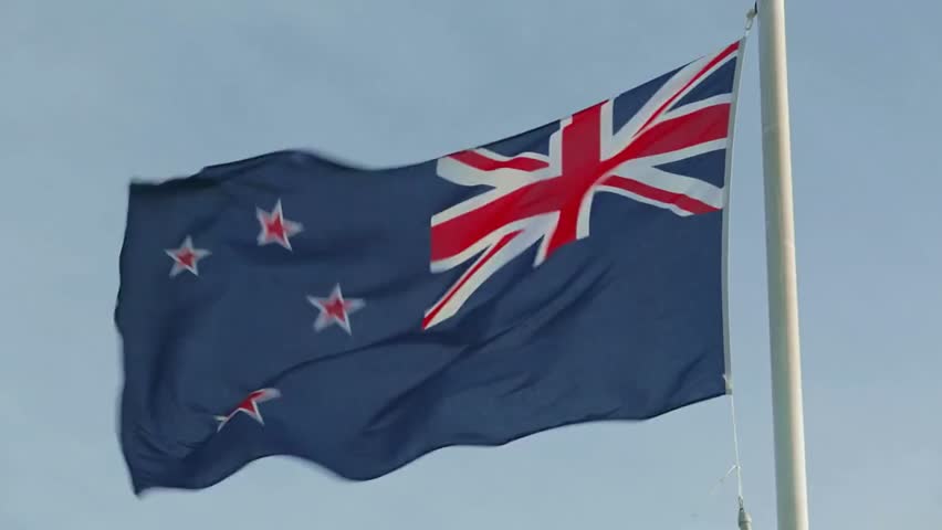 The national flag of New Zealand waving on a white pole, symbolizing patriotism, national pride, and identity in a clear outdoor setting.