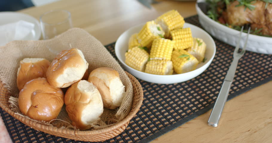 Camera is starting panning across dining table to reveal basket with rolls, corn, roast chicken. Rustic, celebration, family, hospitality, culinary, arrangement, casual