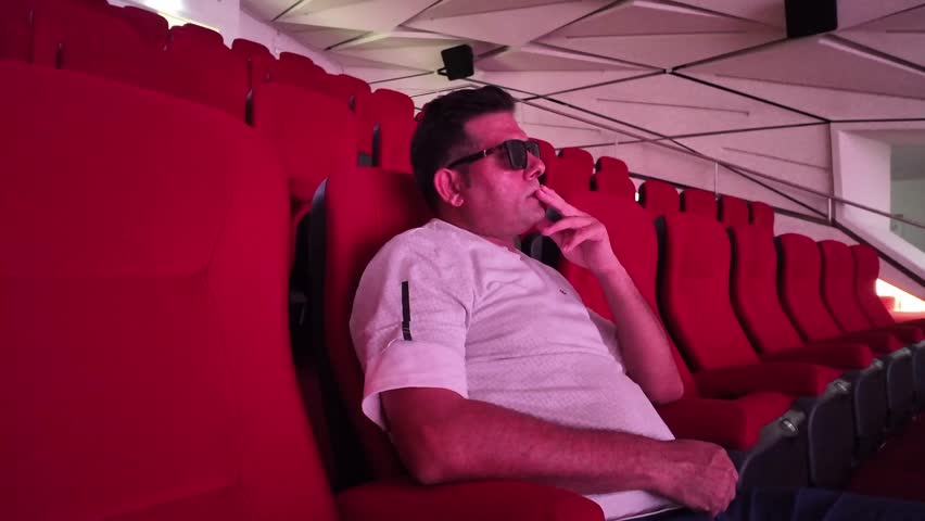 A spacious and darkened cinema hall showcasing rows of empty seats surrounded by a soft, dim projection light