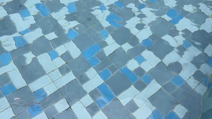 Slow motion video of clear pool water shimmering on blue white mosaic tile floor.