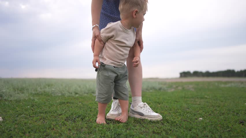 Woman and child standing in a field. Mother holds her baby in the park. Barefoot mom protecting her baby in the sand. A child and a woman are standing in a lifestyle meadow.