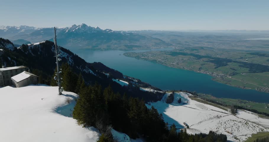An aerial view from Rigi Kulm in Weggis, Switzerland, overlooking snowy slopes descending toward Lake Lucerne, framed by distant peaks and horizons
