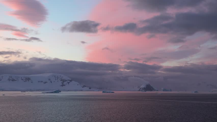 A beautiful sunset paints the sky with shades of orange and purple as the sun sets behind the mountains. Calm waters reflect the stunning colors in this peaceful sea landscape.