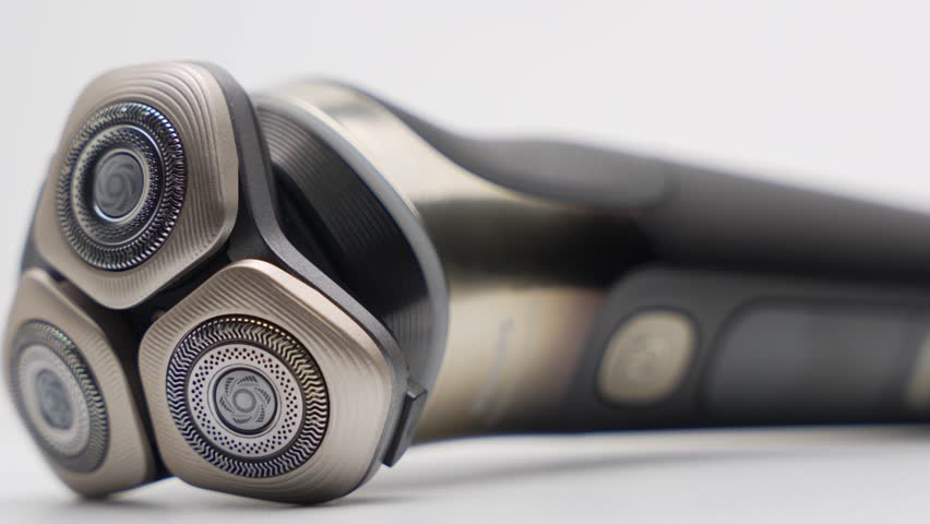 A premium electric rotary shaver slowly rotates on a white background. Macro shot focuses on the triple shaving heads and metallic design.