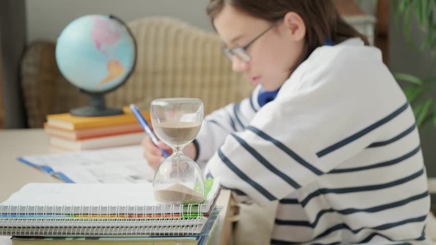 Teenager Student studying doing homework at desk with hourglass, education, knowledge and time management, writing, learning process, exam prep, child training, concentration and discipline sand timer - Powered by Shutterstock - Get 15% off with code: PIKWIZARD15
