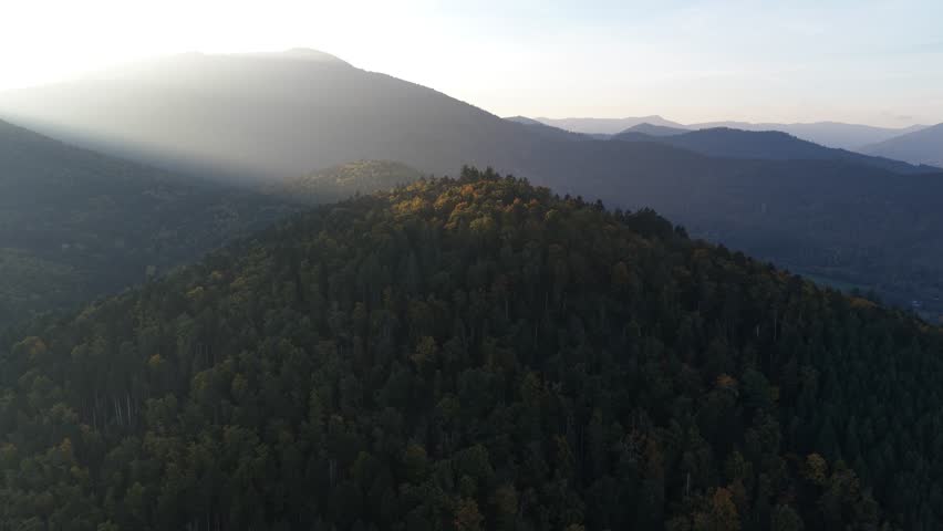 An aerial view of sunbeams cutting across the forested peaks of the Massif des Maures in Provence, France, creating a breathtaking natural landscape