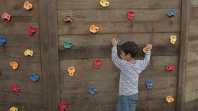 Asian boy climbing colorful rock wall on wooden playground, outdoor activity and childhood development - Powered by Shutterstock - Get 15% off with code: PIKWIZARD15