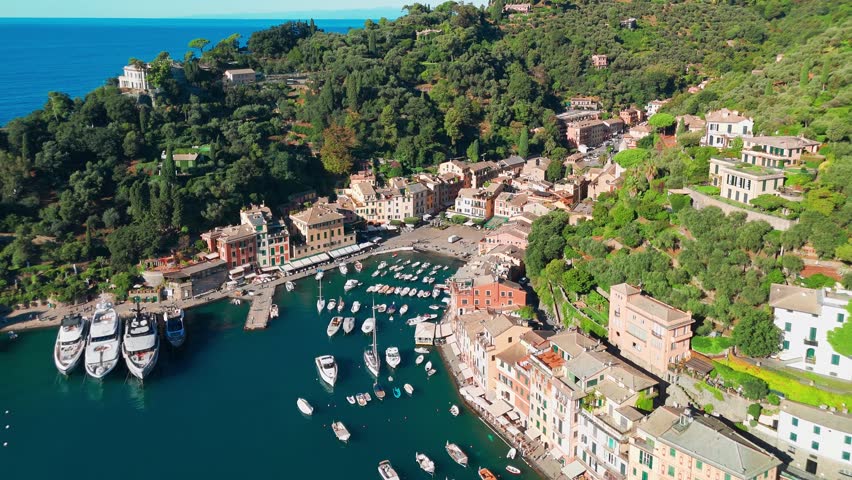 Aerial view of the picturesque resort town of Portofino in Liguria, Italy. Charming harbour with moored sailboats and luxury yachts surrounded by historic colorful buildings along the Ligurian coast.