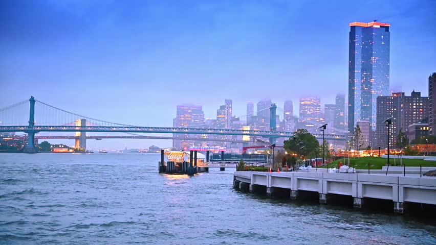 Moving on boat along the beautiful waterfront at dusk time. The Manhattan Bridge and New York city skyline at backdrop.