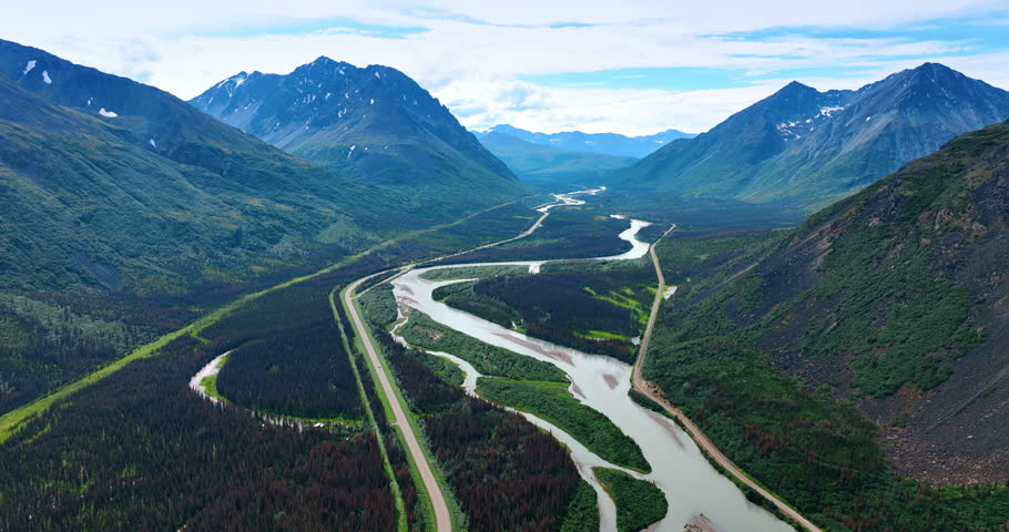 Branching river and a highway along it crossing the gorgeous valley at the mountain foot. Drone footage over the spectacular nature landscape of Alaska.