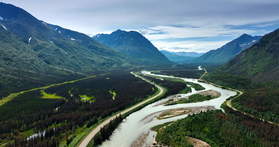 Valley among the spectacular mountain is overgrown with pine tree woods. A branching river is crossing the landscape. Aerial view. Alaska, USA.