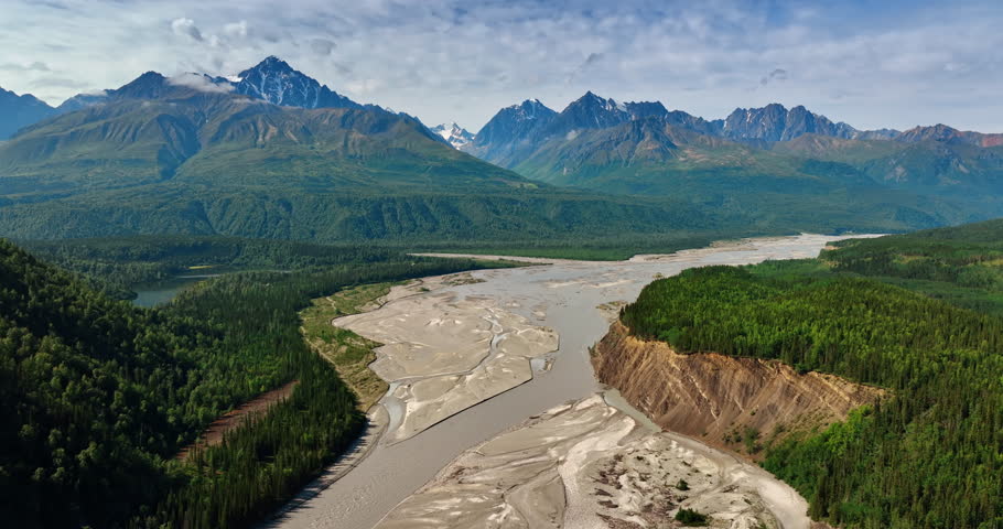Flight over the wide delta of the shallow river in Alaska wilderness. Gorgeous ridged mountains at backdrop.