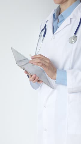 Unknown female doctor, wearing white coat over a blue blouse and a stethoscope, is using a digital tablet, suggesting innovative healthcare practices in medicine. Health care and medicine concept