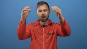 Man in orange prisoner jumpsuit holding head with both hands in a studio blue setting, inmate number visible; anxiety. - Powered by Shutterstock - Get 15% off with code: PIKWIZARD15