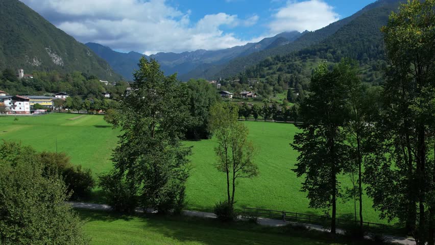 Aerial panorama of bright green meadows scattered village houses and surrounding steep mountain slopes in the Valle di Ledro region on a sunny clear day near Bezzecca

