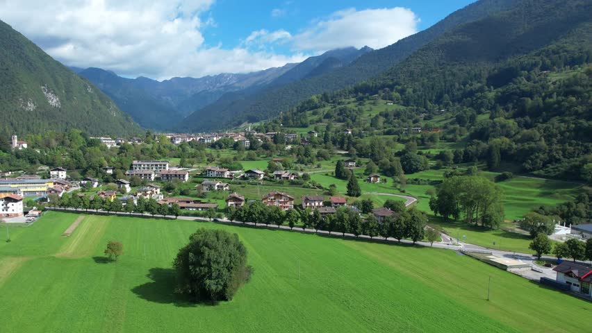 Aerial view of green valley fields village houses and surrounding mountain slopes in the Valle di Ledro region on a bright sunny day near Bezzecca
