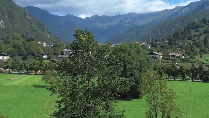 Aerial view of green meadows village rooftops and surrounding mountain slopes near Bezzecca in the Valle di Ledro region on a sunny clear day
